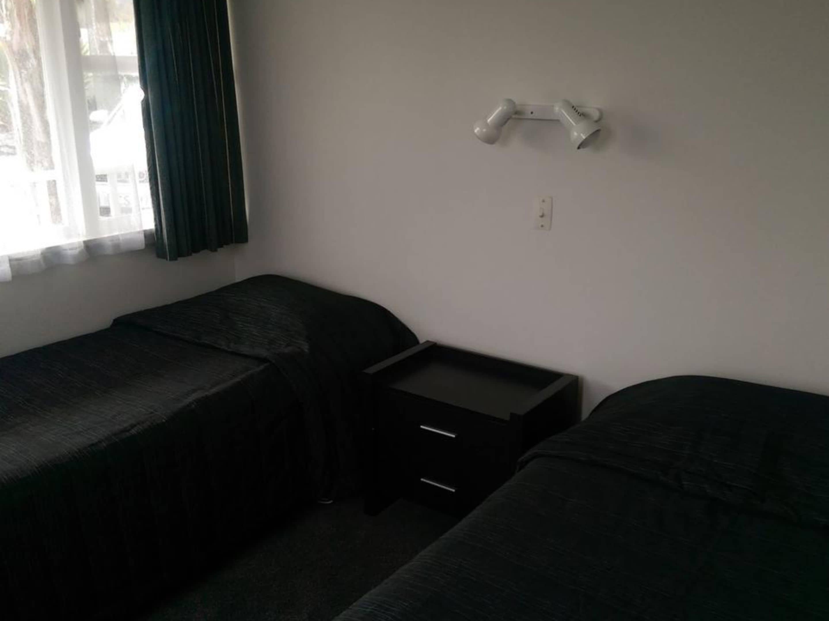 A small, dimly lit room with two single beds, a small desk, and a window with curtains.
