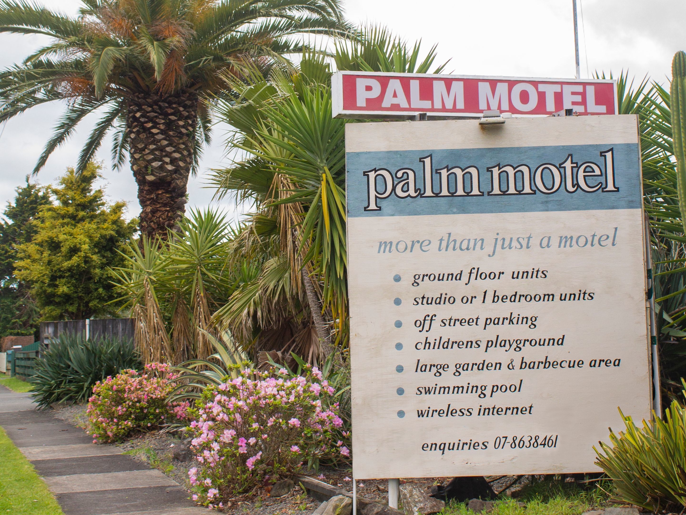 Letrero del motel Palm que anuncia comodidades como habitaciones en la planta baja, estudios o unidades de un dormitorio, estacionamiento fuera de la calle, parque infantil, un jardín y área de barbacoa amplios, piscina e internet inalámbrico.