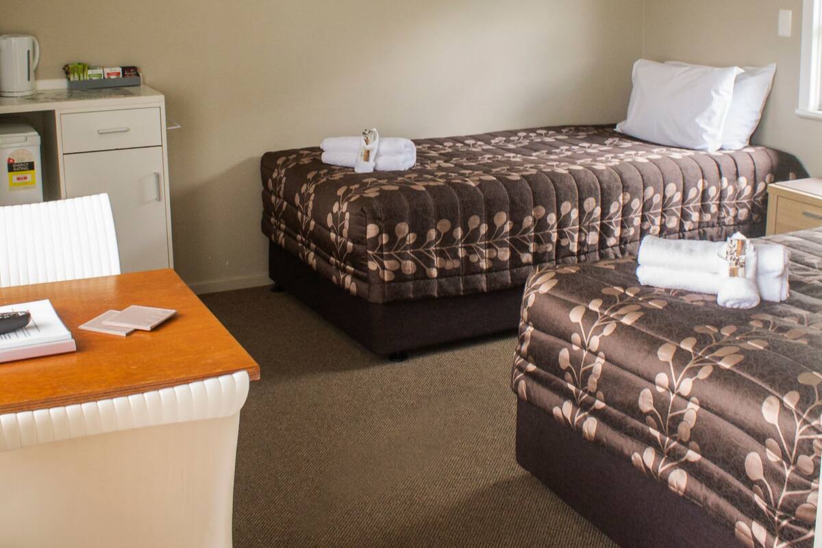 A hotel room with two beds, a desk, and a chair. There are towels on the beds and a coffee maker on the desk.