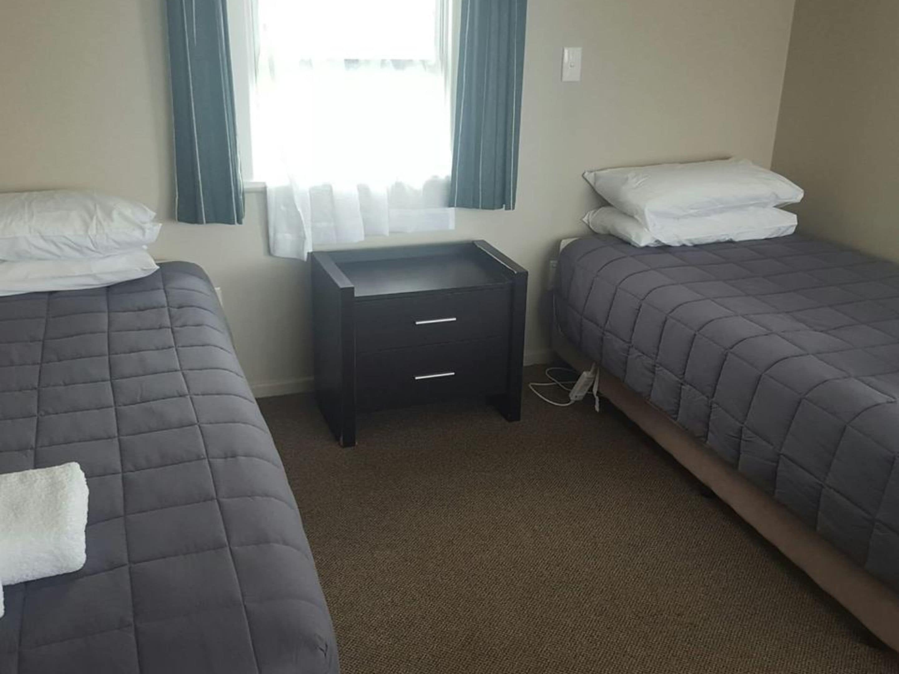 Habitación de hotel con dos camas, una mesita y una ventana con cortinas.