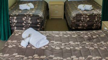 A hotel room with two single beds, each with a floral-patterned bedspread and a folded towel. There is a wooden nightstand between the beds.