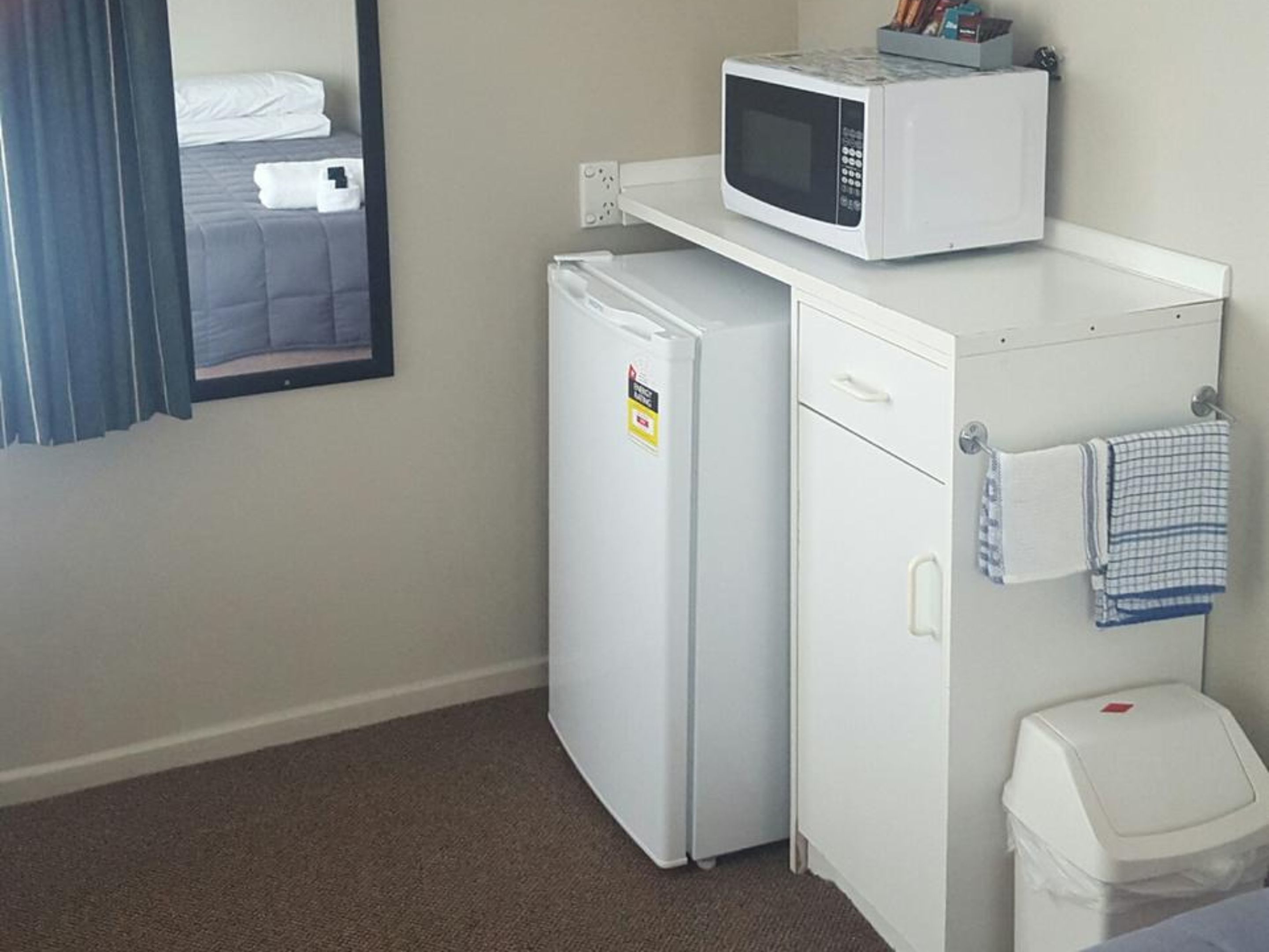 Una habitación de hotel compacta con kitchenette, que incluye un refrigerador, microondas y un pequeño cubo de basura.