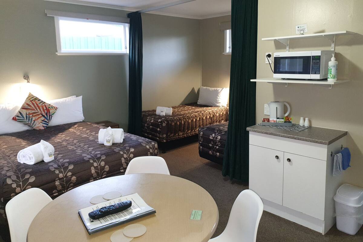 A hotel room with two beds, a small kitchenette, a dining area, and a window with curtains.