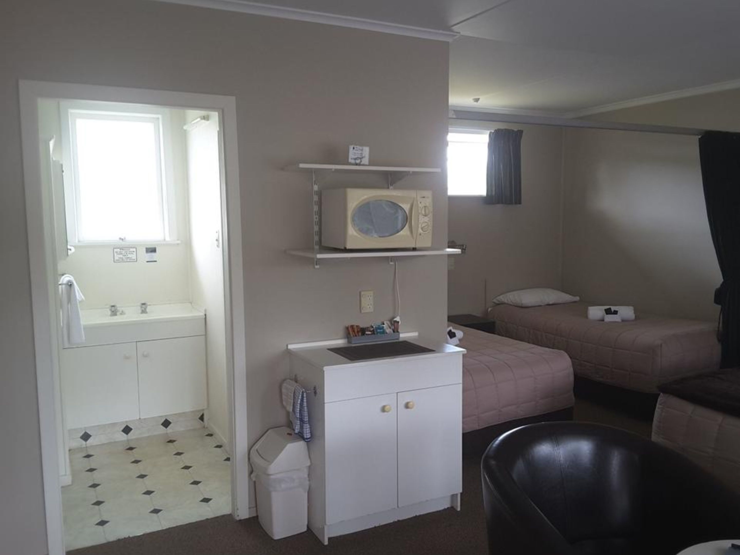 A hotel room with a bathroom, a microwave, a bed, and a small table.