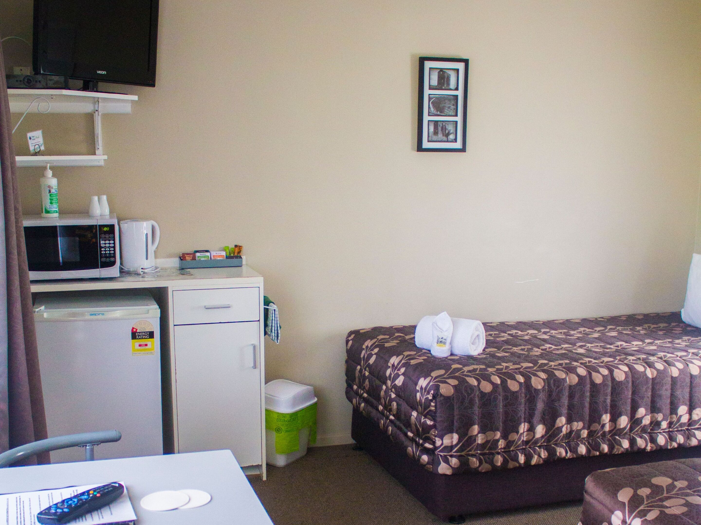 A hotel room with a bed, a desk with a microwave, a TV, and a trash bin.