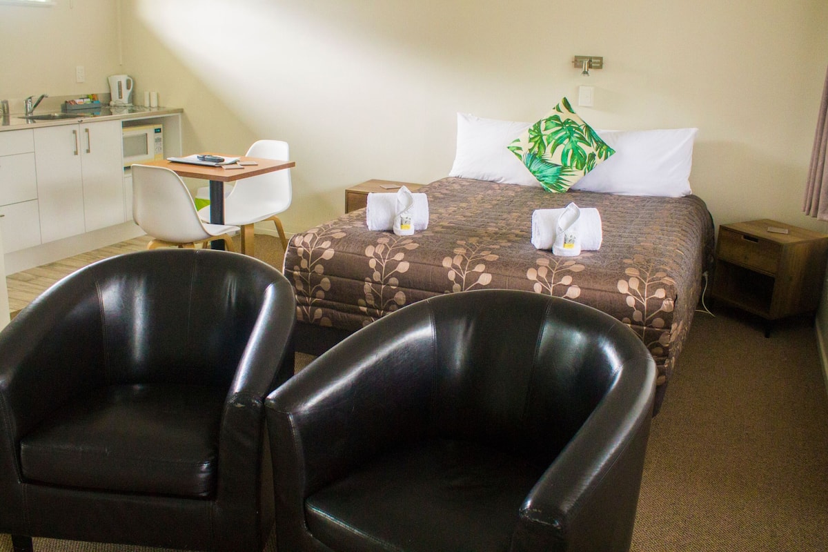 A hotel room with a bed, two chairs, a desk, and a small table.