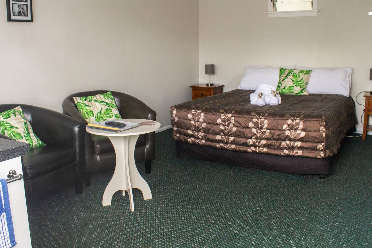A hotel room with a bed, two chairs, a small table, and a nightstand.