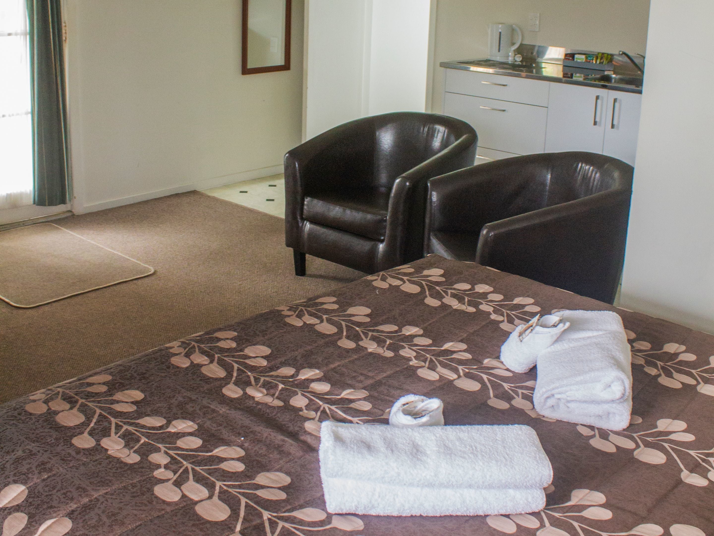Una habitación de hotel con una cama, dos sillones de cuero, una kitchenette pequeña y un baño.
