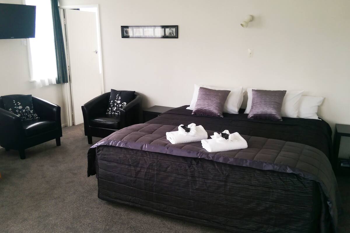 A hotel room with a large bed, two armchairs, a small table, and a wall-mounted picture.