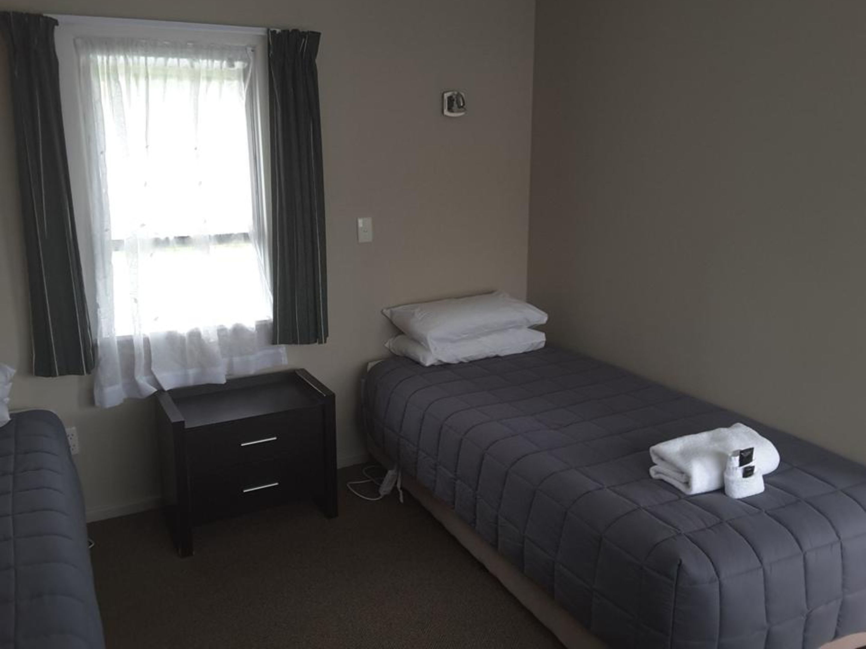 A small, clean room with a single bed, a bedside table, and a window with curtains.