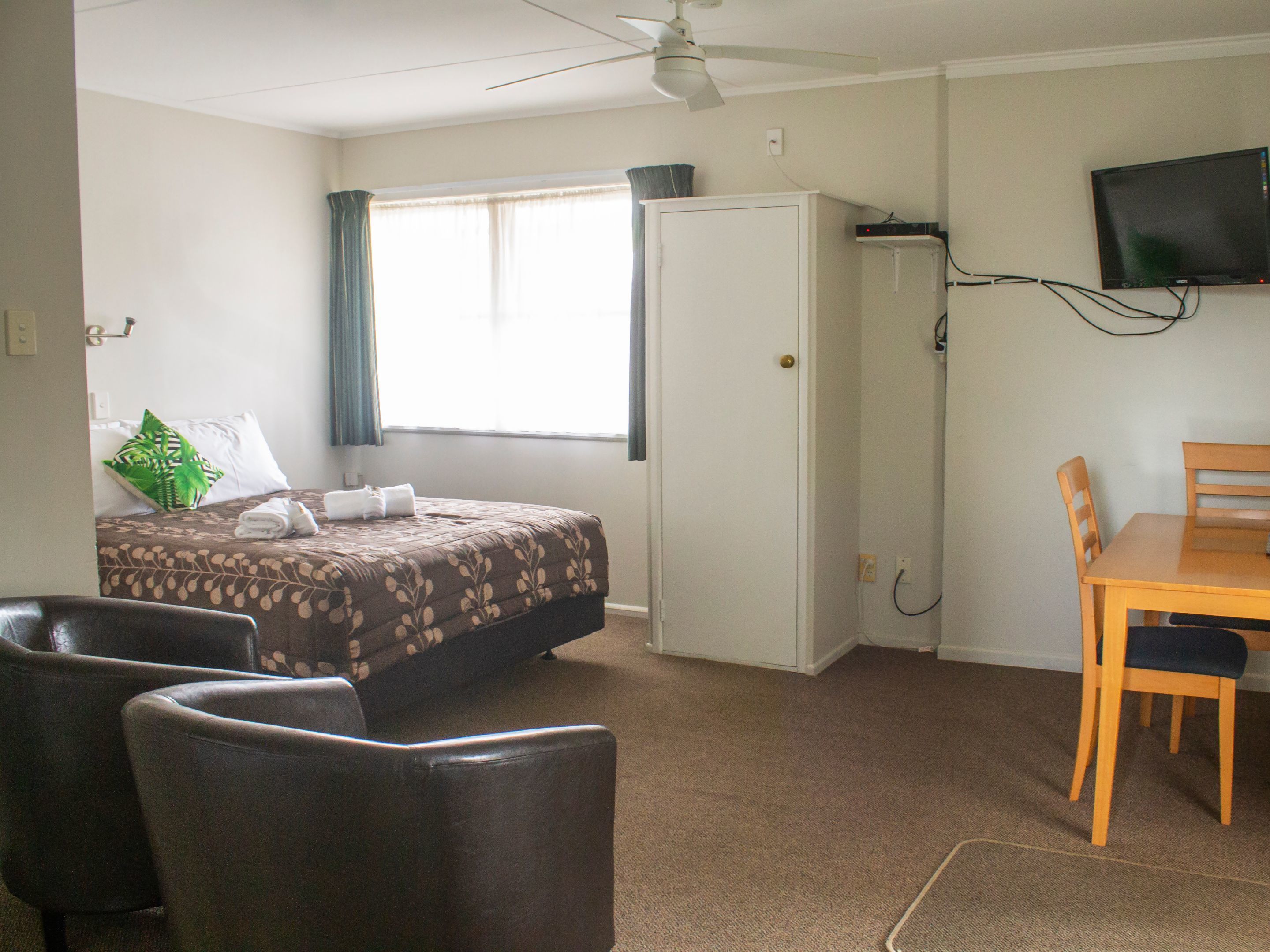 A hotel room with a bed, a desk, a chair, a television, and a ceiling fan.