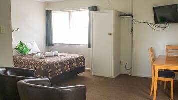 A hotel room with a bed, a desk, a chair, a television, and a ceiling fan.