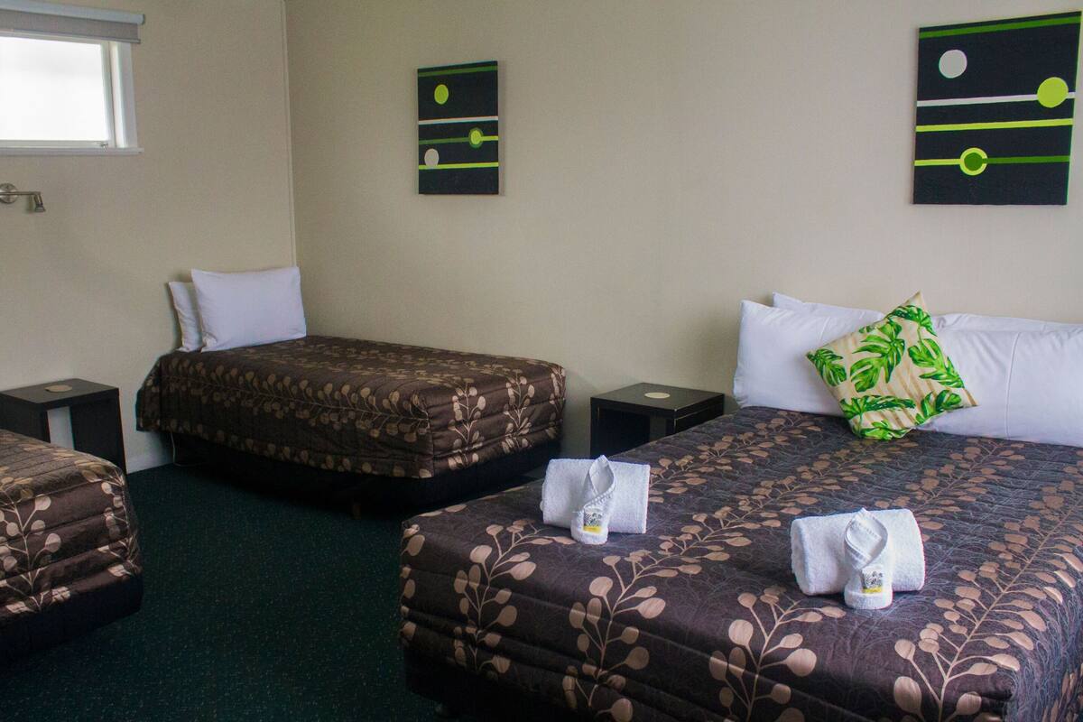 A hotel room with two beds, a nightstand, a small table, and artwork on the walls.