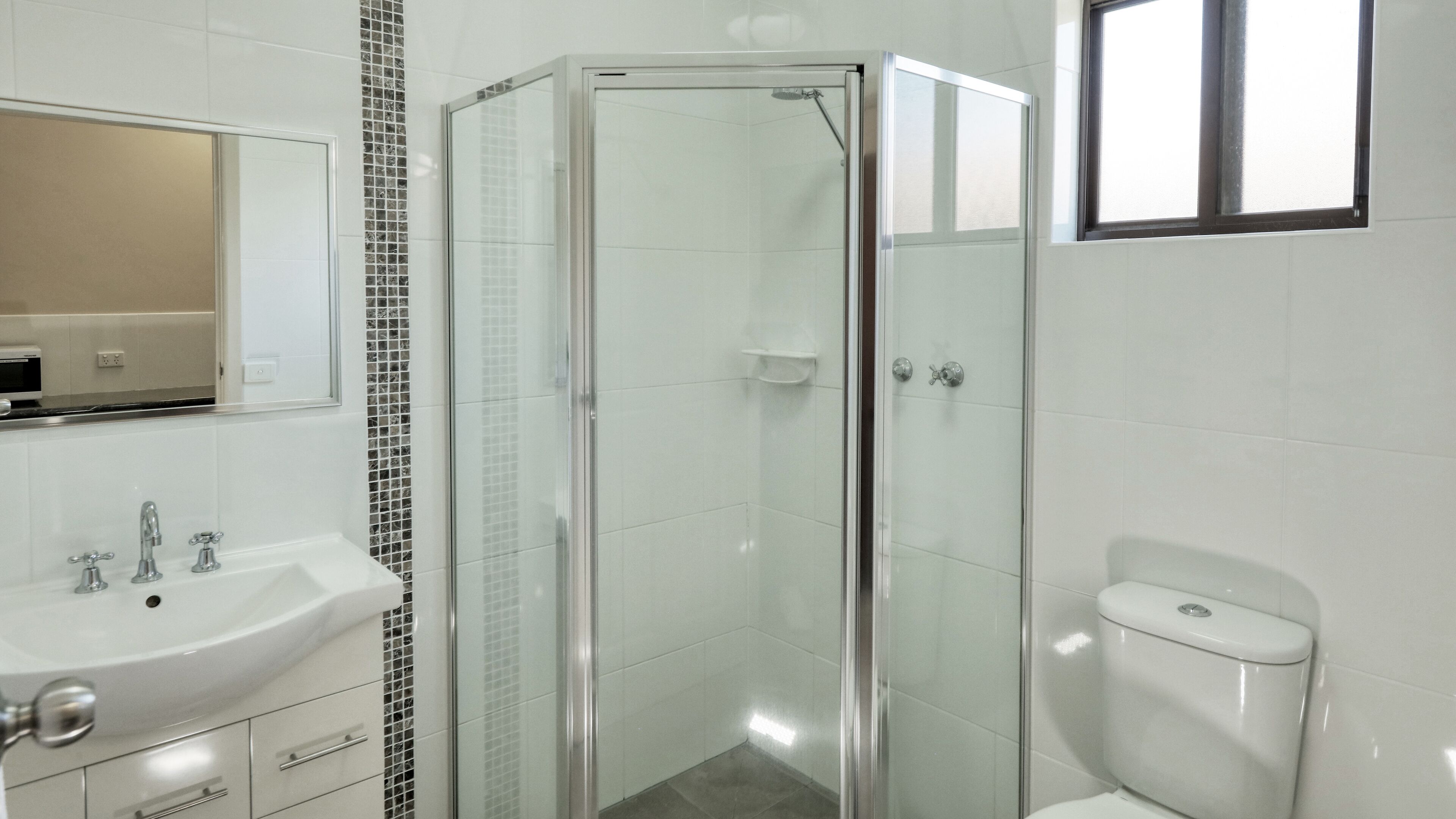 A modern bathroom with a glass-enclosed shower, a white sink with a mirror above it, and a toilet.