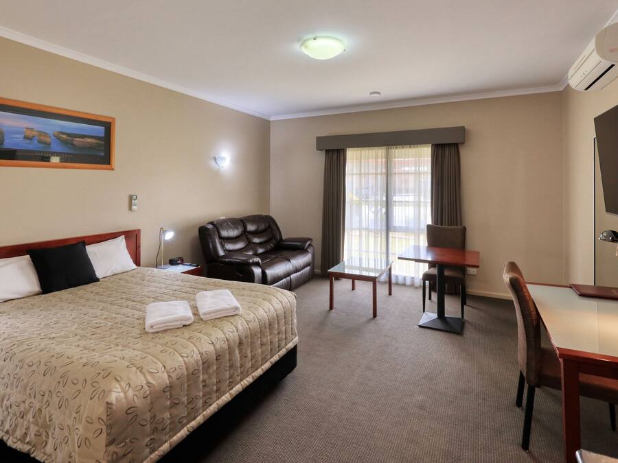 Habitación de hotel con una cama grande, un escritorio, una silla, un sofá de cuero, un televisor y una ventana con cortinas.