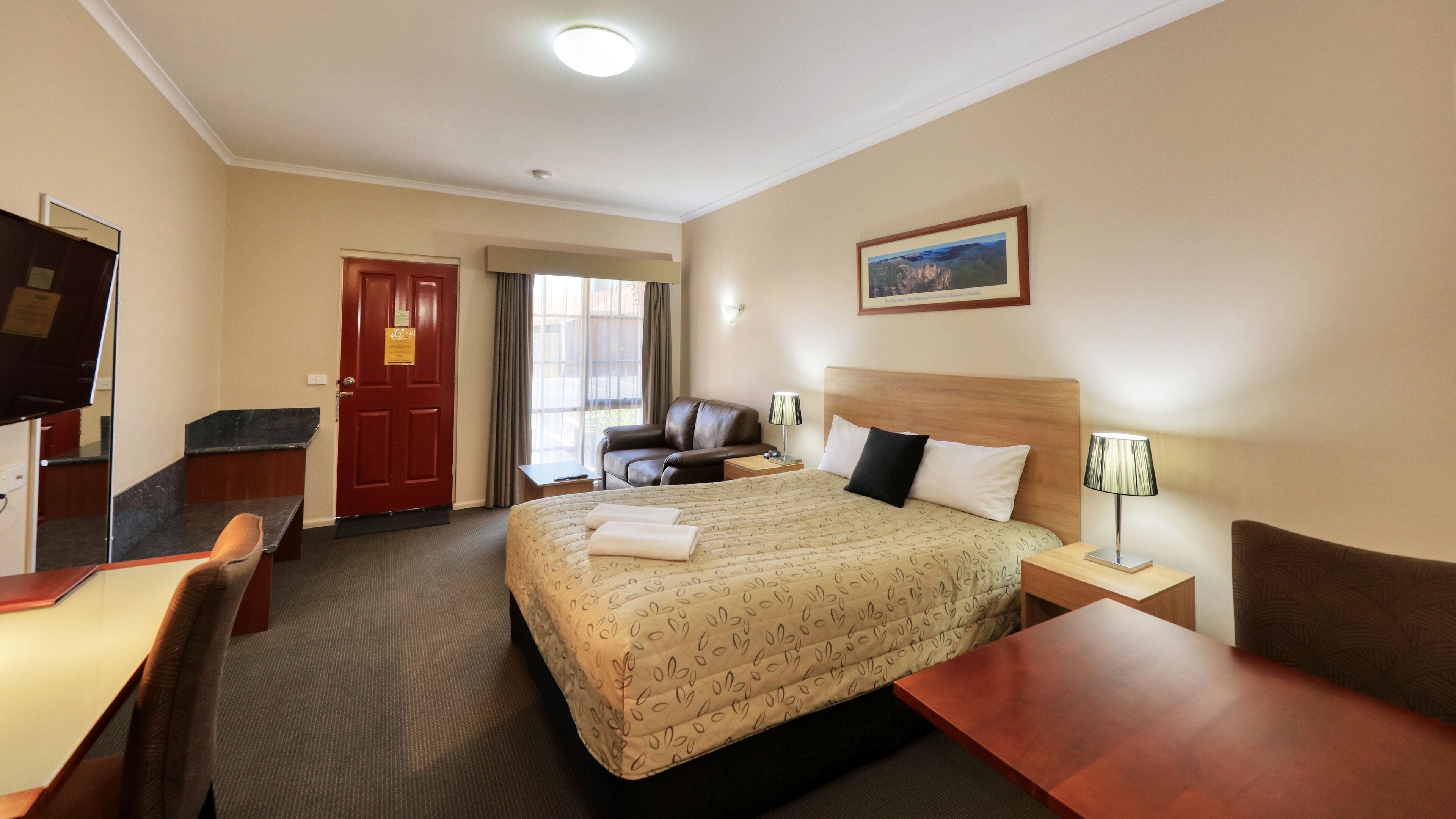 Ein Hotelzimmer mit Bett, Schreibtisch, Stuhl, Fernseher, Tür und einem Fenster mit Vorhängen.