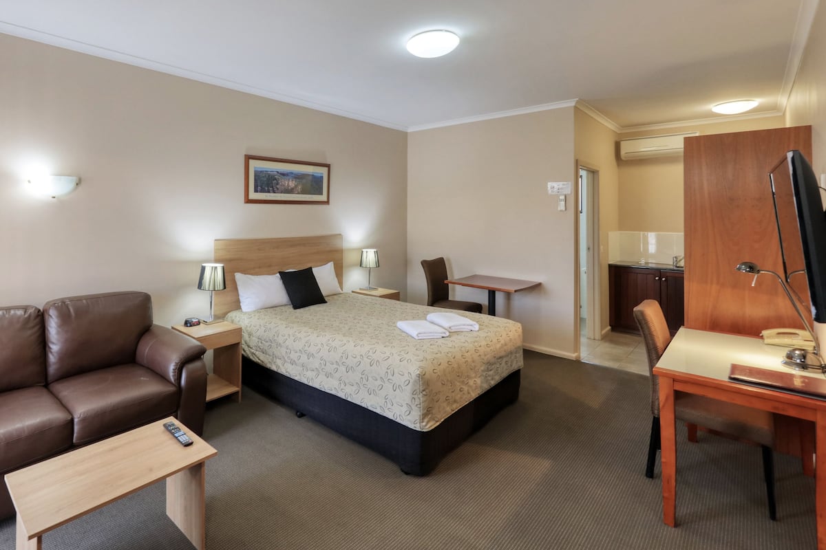 Une chambre d’hôtel avec un lit, un fauteuil en cuir marron, un bureau, une petite table et une lampe de bureau.