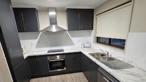 A modern kitchen with dark cabinets, a stainless steel range hood, a built-in oven, a dishwasher, and a marble countertop. - Top of the Town Motel & Apartments (Benalla)