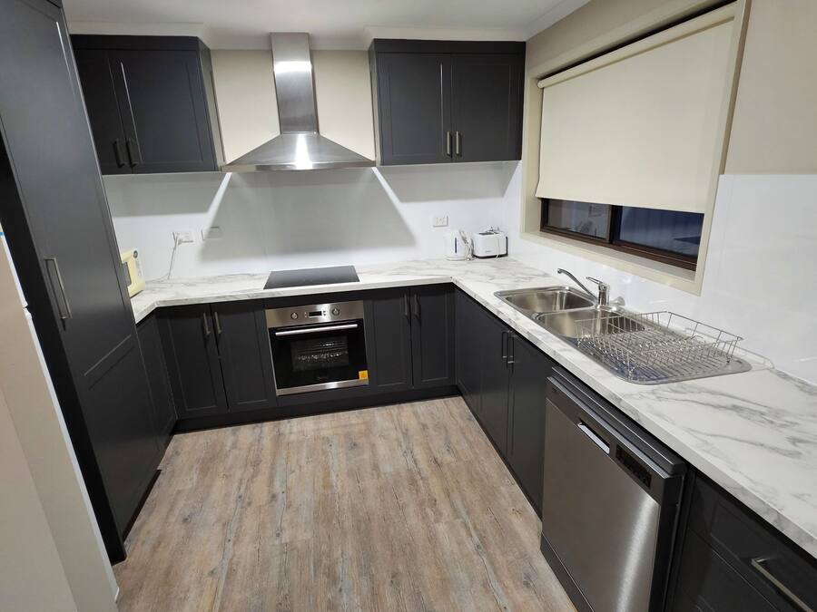 A modern kitchen with dark cabinets, a stainless steel range hood, a built-in oven, a dishwasher, and a marble countertop.