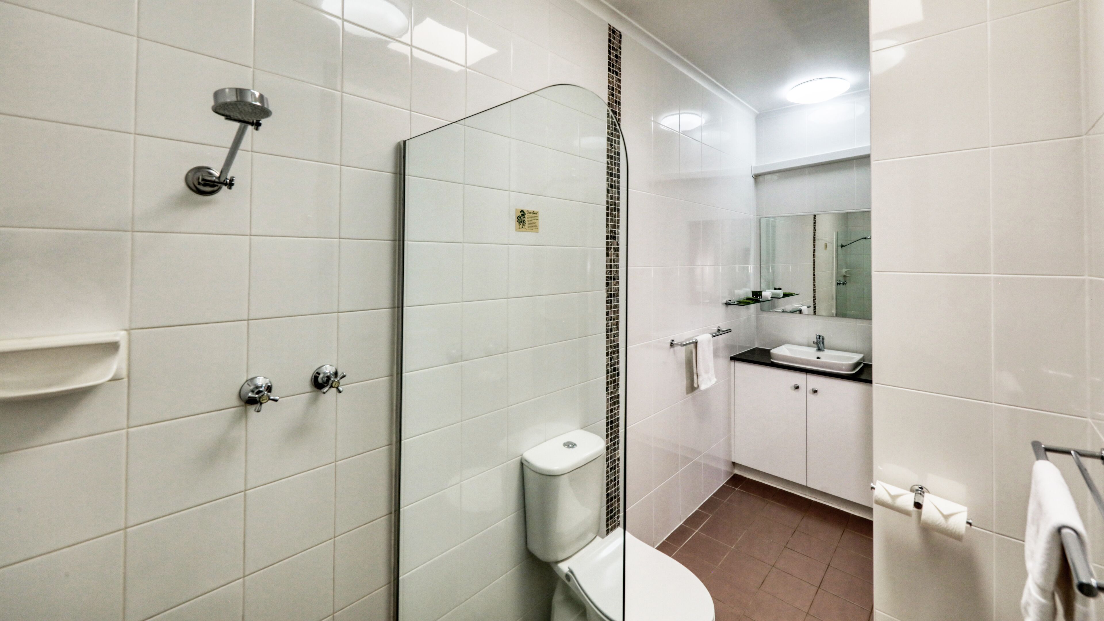 Un bagno moderno con cabina doccia in vetro, un water, un lavandino e uno specchio.
