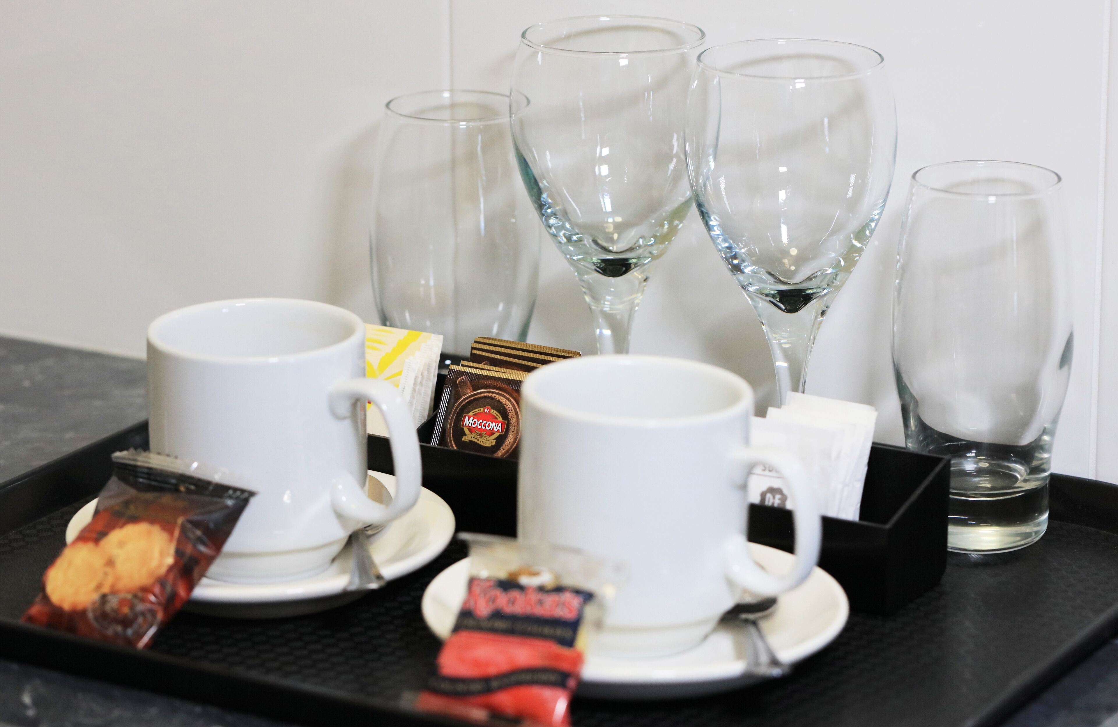 Una bandeja con tazas de café, una tetera y paquetes de aperitivos.