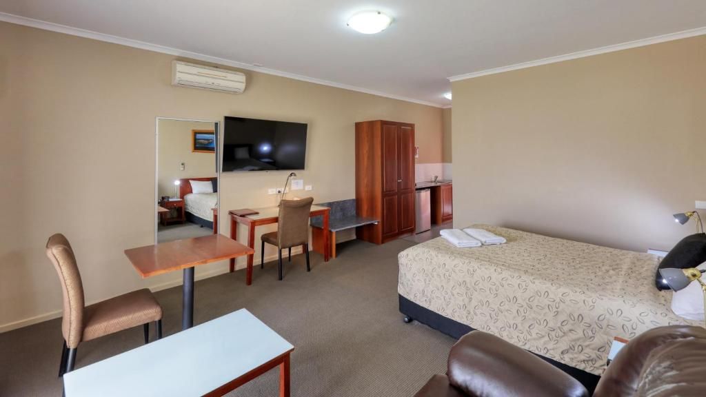 A hotel room with a bed, a desk, a chair, a television, and a wardrobe.