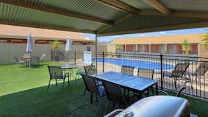 A covered outdoor area with a pool, a barbecue grill, and a table with chairs. - Top of the Town Motel & Apartments (Benalla)