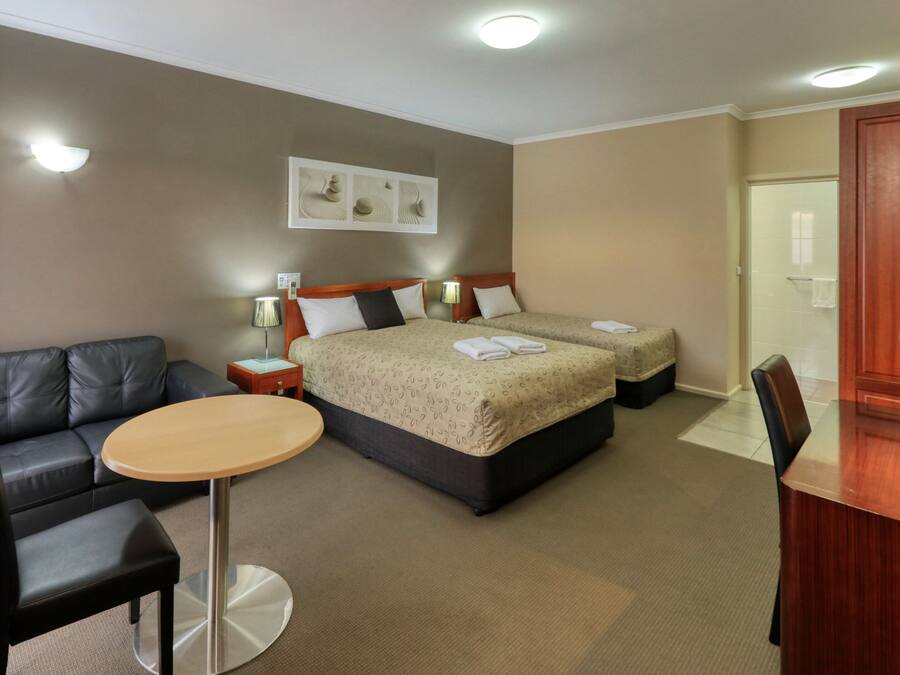 Quarto de hotel com uma cama, um sofá, uma mesinha e uma televisão.