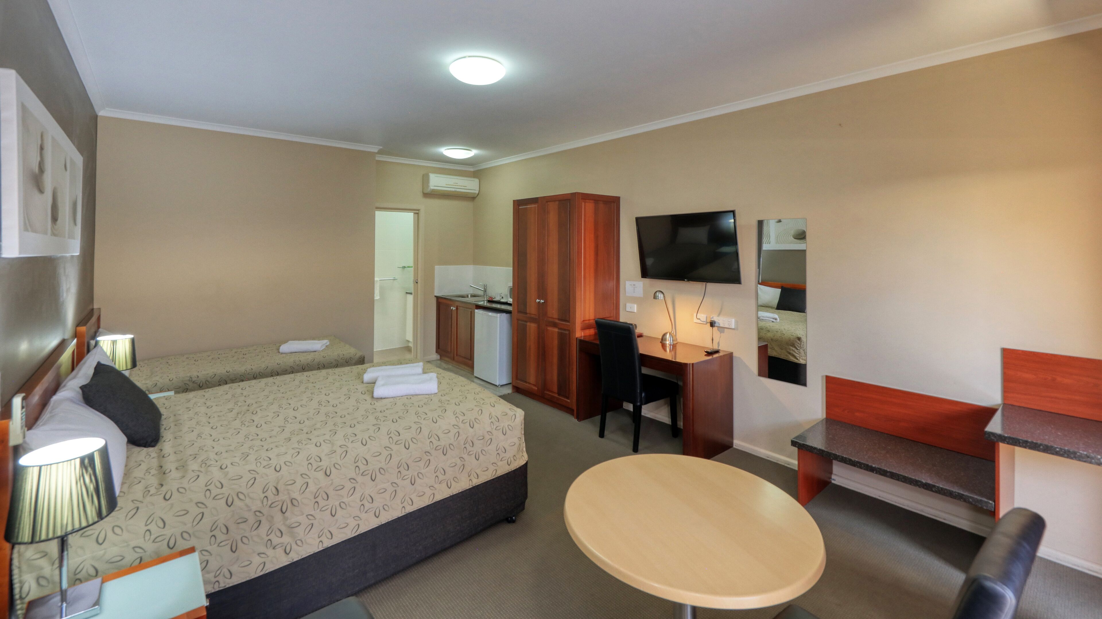 A hotel room with two beds, a desk, a chair, a small table, a TV, and a wardrobe.