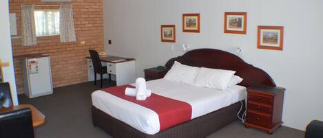 Una habitación de hotel con cama, escritorio, silla, cómoda y refrigerador.