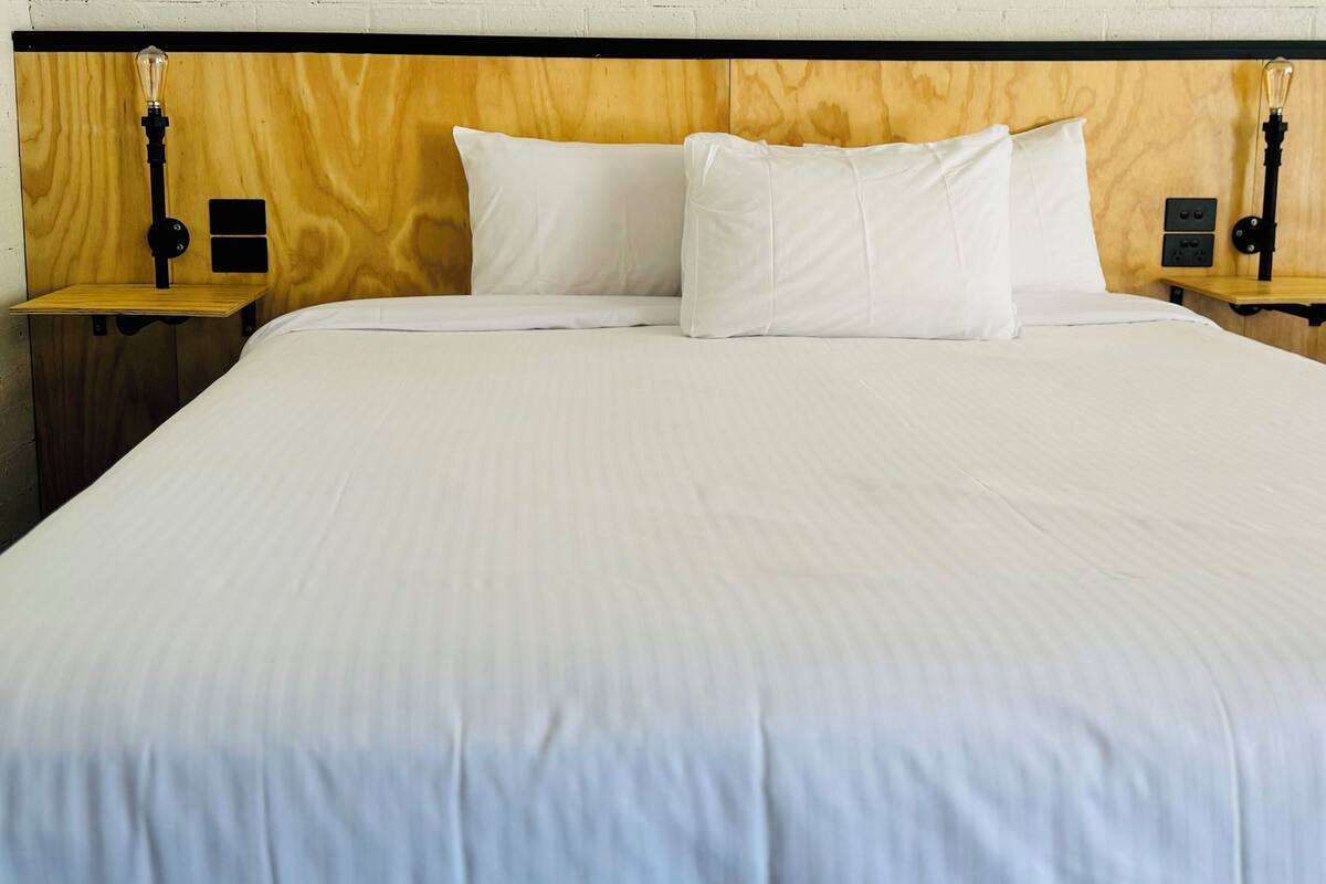 A bed with white linens, two bedside tables with lamps, and a wooden headboard.