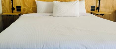 Una cama con sábanas blancas, dos mesitas de noche con lámparas y un cabecero de madera.