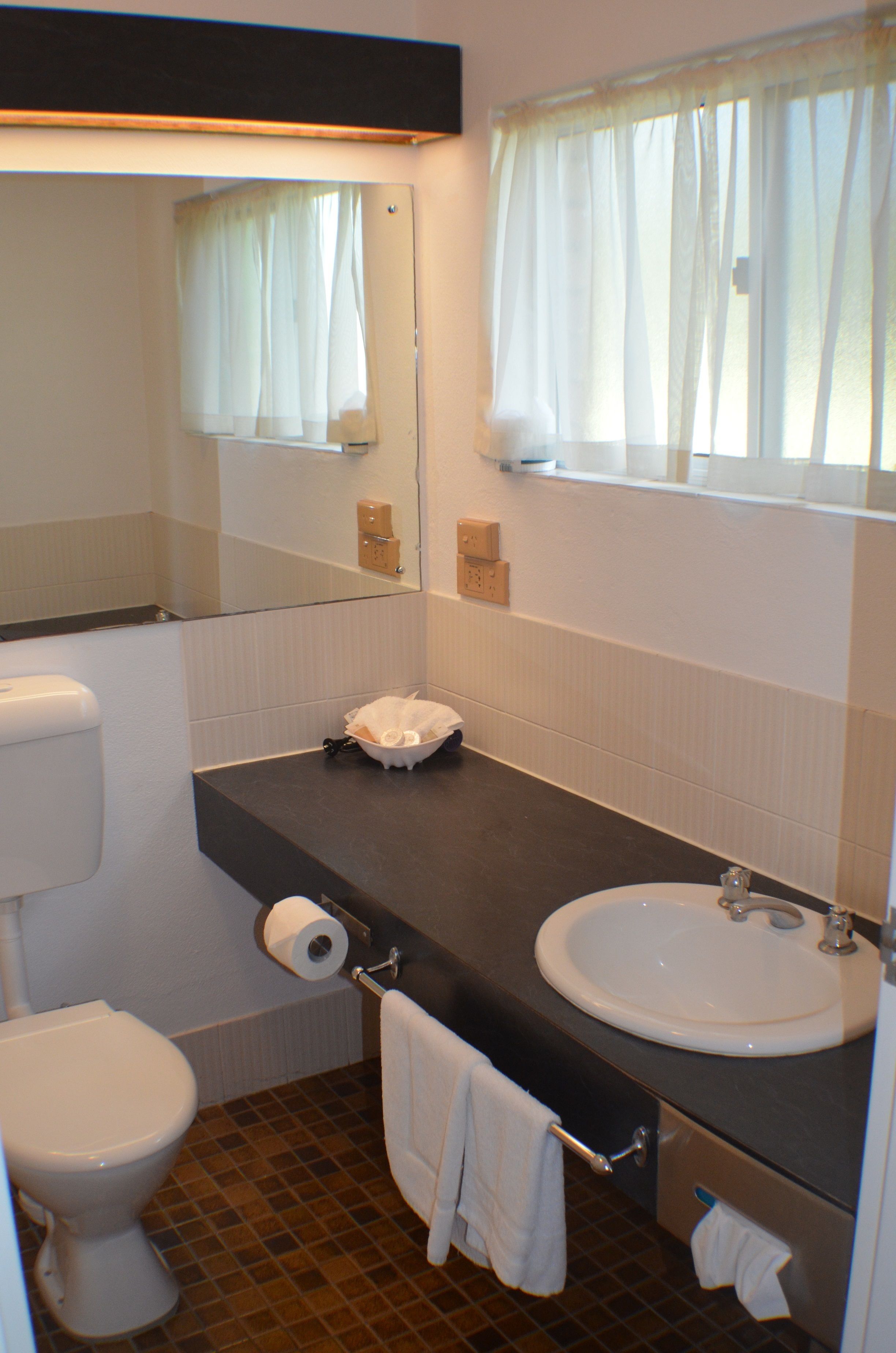 Un baño con inodoro, lavamanos, espejo y toallero.