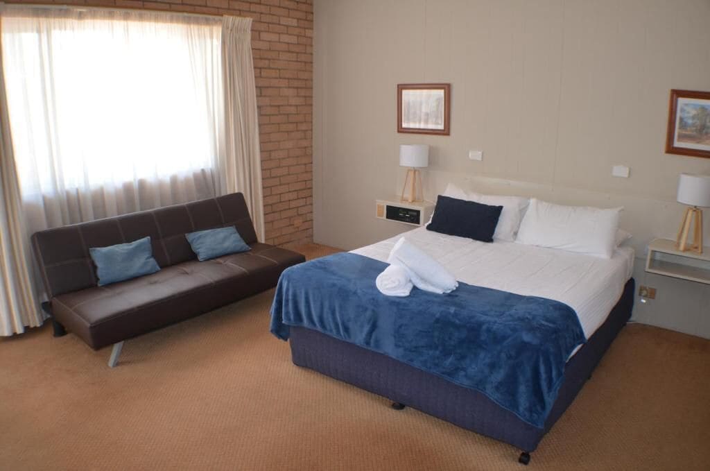 Ein Hotelzimmer mit Bett, Sofa, zwei Nachttischen und einem Fenster mit Vorhängen.