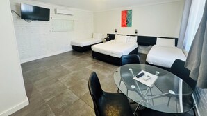 Ein Hotelzimmer mit zwei Betten, einem Fernseher, einem Glastisch und einem roten abstrakten Gemälde an der Wand.