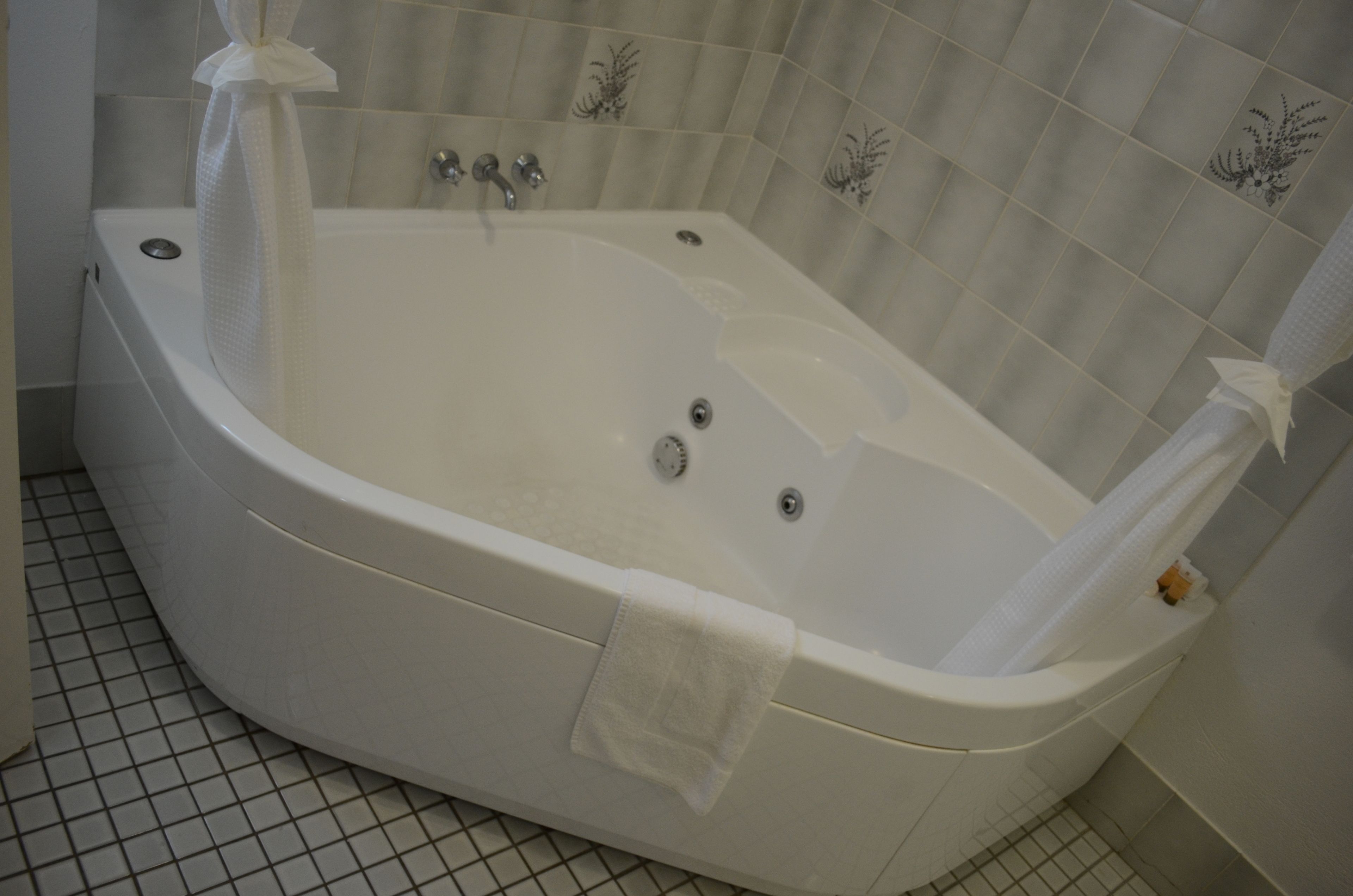 Una bañera blanca independiente con cortina de ducha, una toalla y un panel de control.