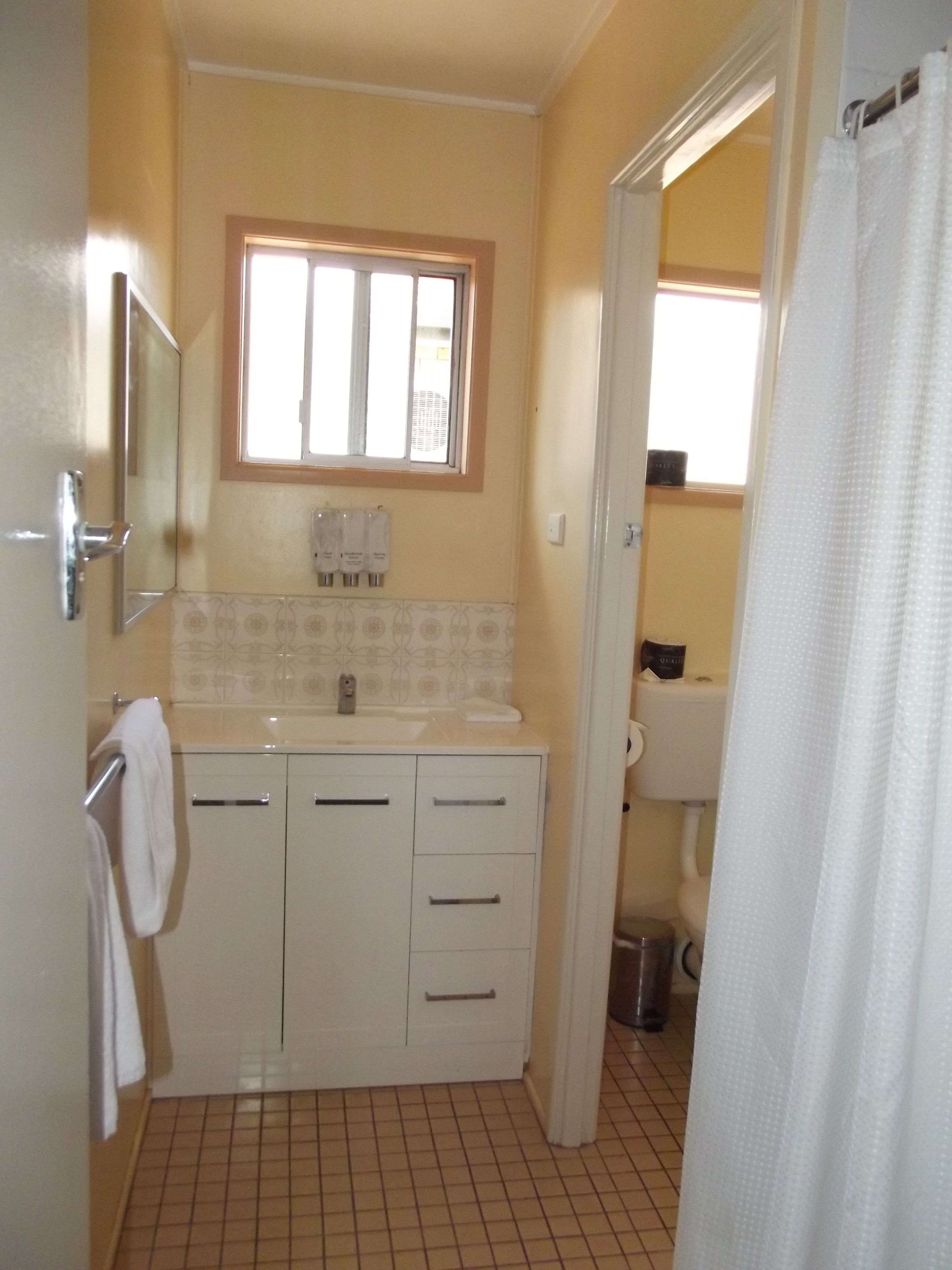 Casa de banho com lavatório branco, dois armários, um espelho e uma janela acima do lavatório.