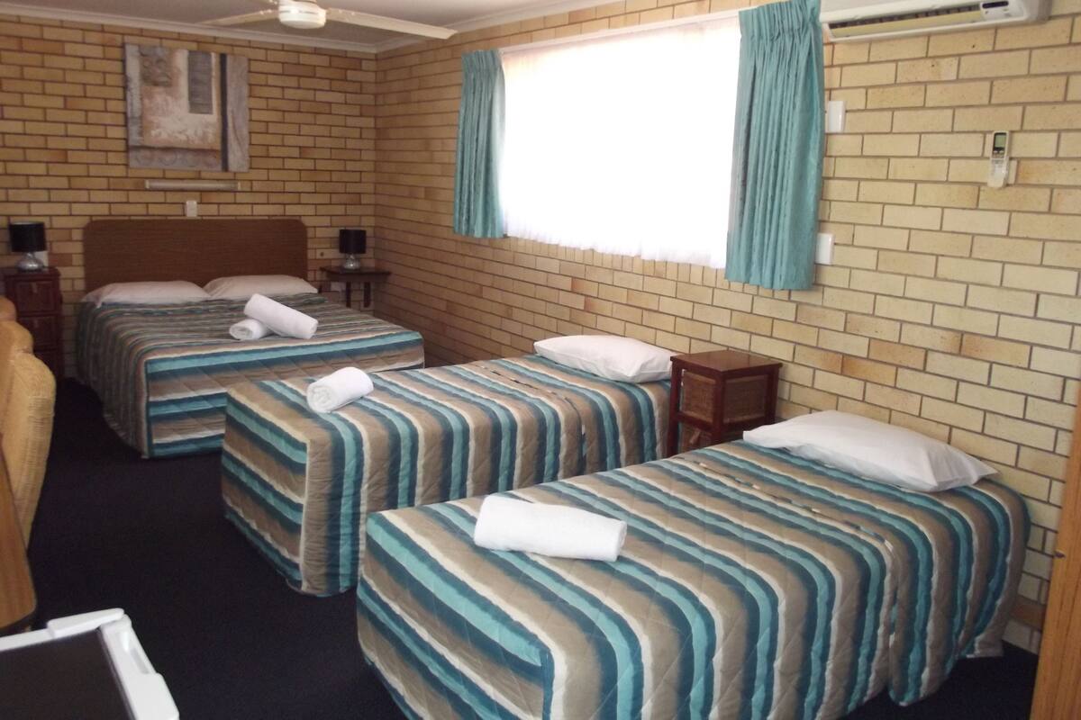 A hotel room with two single beds, a ceiling fan, an air conditioning unit, and a brick wall.