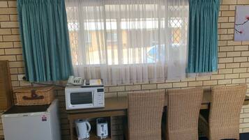 Ein kompakter Raum mit Backsteinwand, einem Fenster mit türkisfarbenen Vorhängen, einer Mikrowelle, einem Toaster und Korbsesseln.