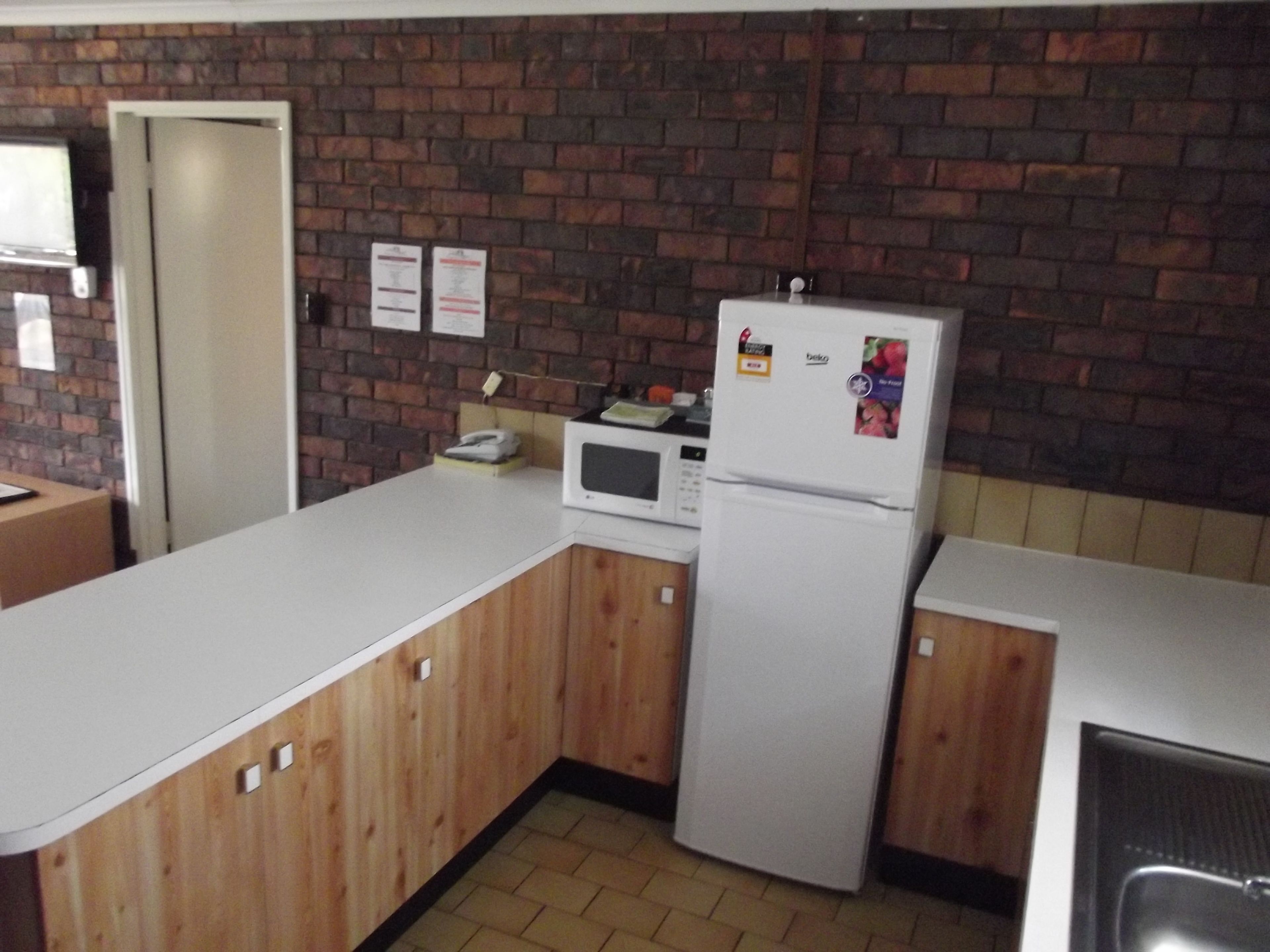 Una cocina con armarios de madera, un refrigerador blanco, un microondas y una pared de ladrillo.