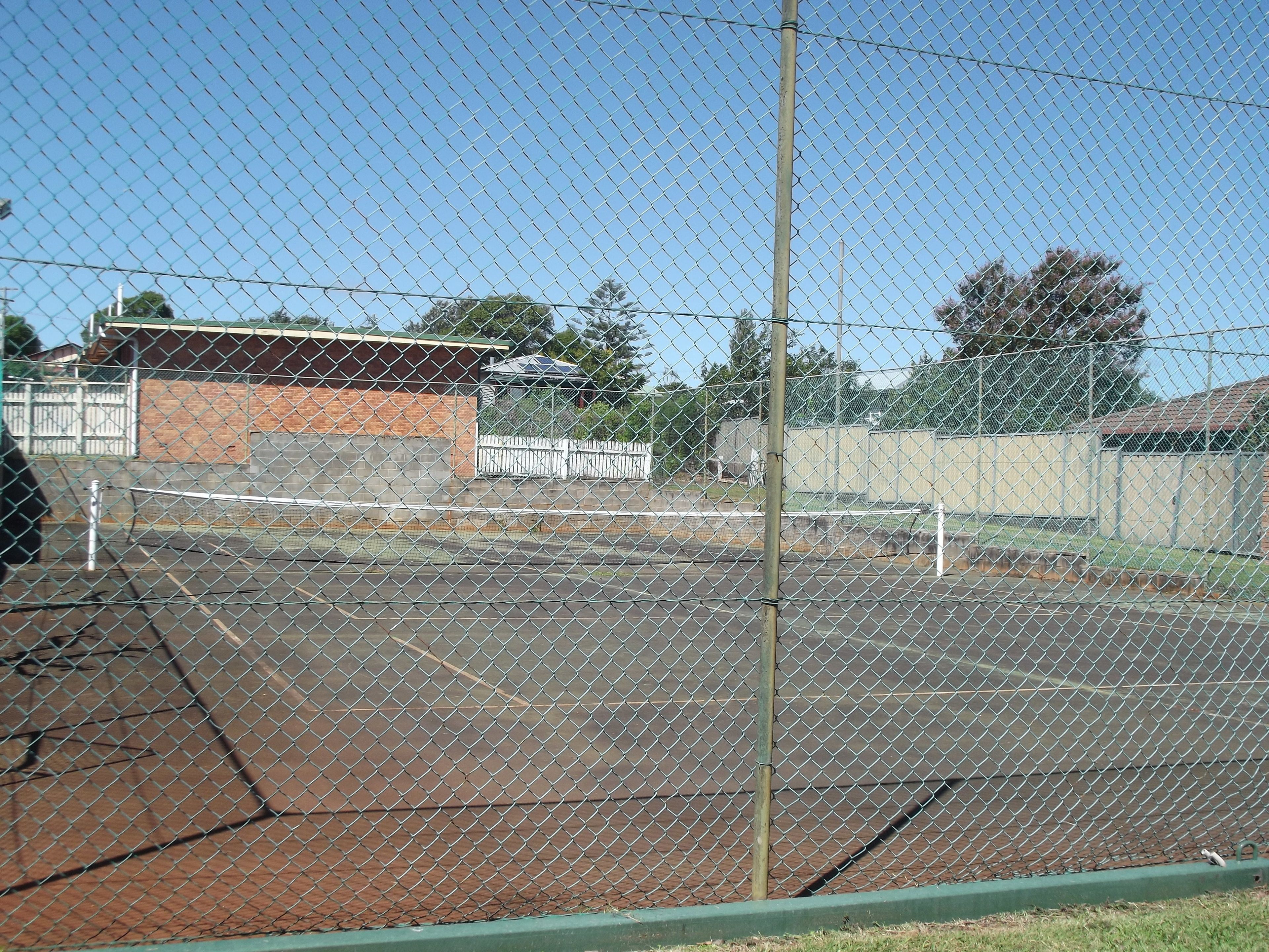 Een omheind tennisveld met een bakstenen gebouw op de achtergrond.