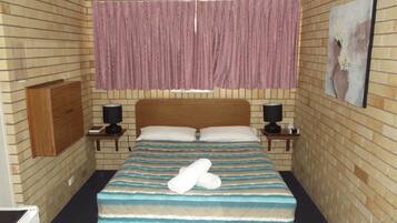 A hotel room with a bed, two bedside tables, a ceiling fan, a window with curtains, and a wall-mounted artwork.