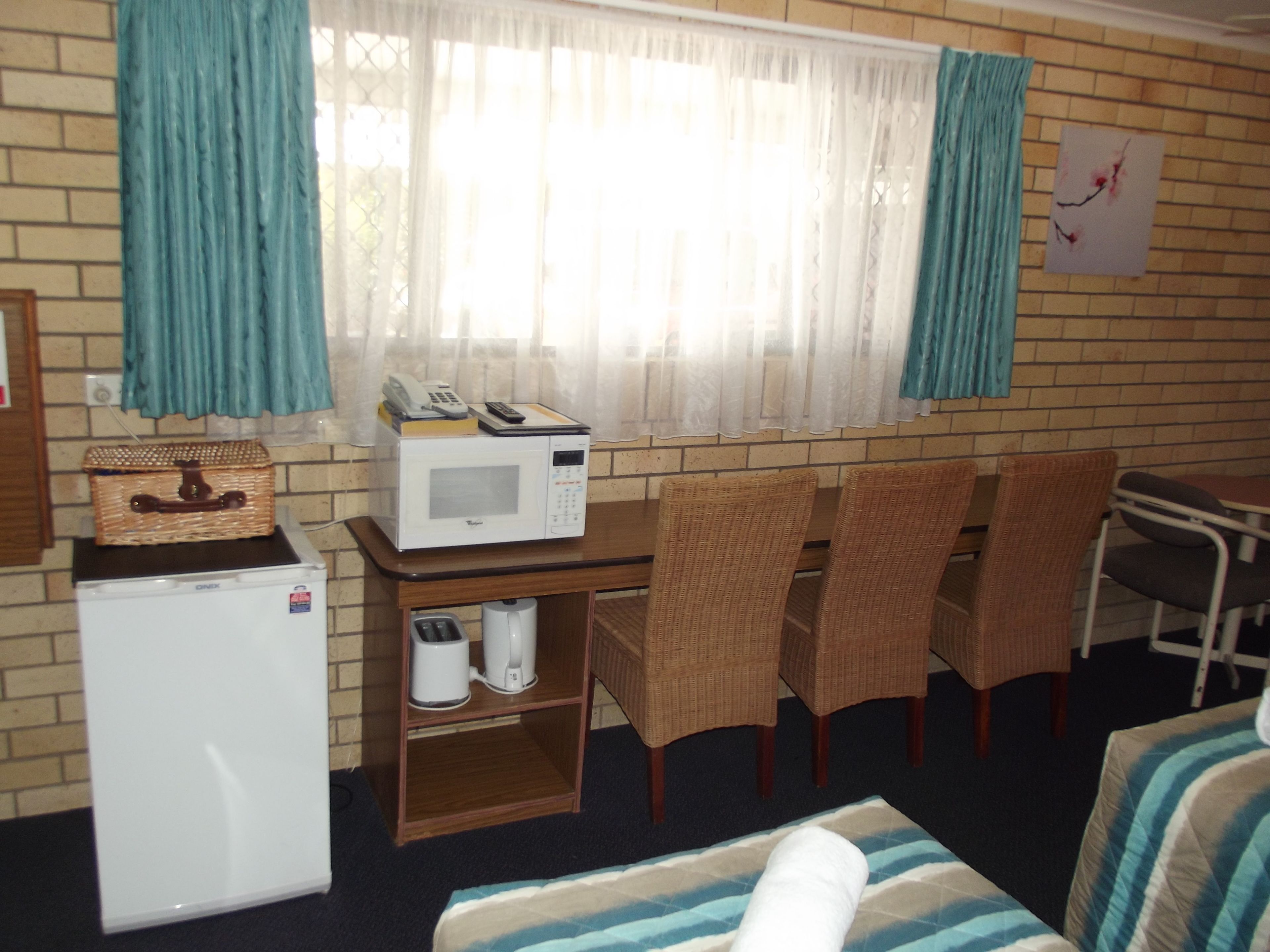 Habitación compacta con kitchenette, microondas, pequeño refrigerador, sillas de mimbre y una mesa de comedor.