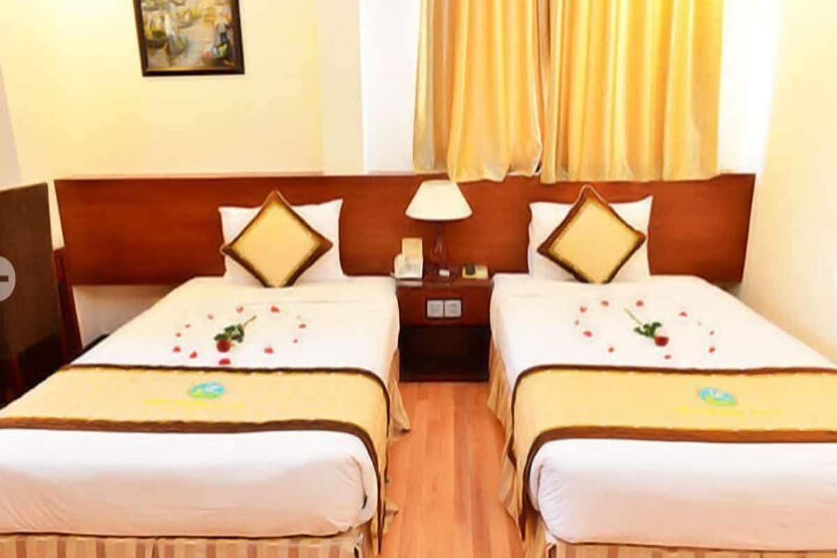 A hotel room with two beds, a nightstand, a lamp, and a painting on the wall.
