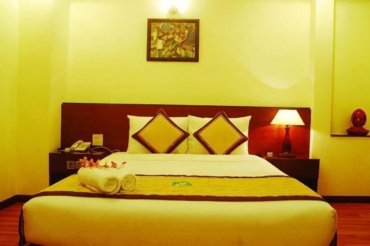 Habitación de hotel con cama, mesita de noche, lámpara y un cuadro en la pared.