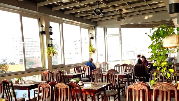 Un restaurante con mesas y sillas de madera, ventanas amplias y ventiladores de techo.