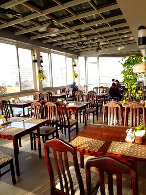 A restaurant with wooden tables and chairs, large windows, and ceiling fans. - Hau Giang Hotel (Can Tho)