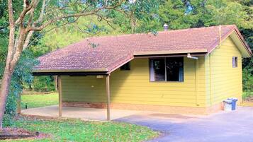A small yellow building with a red-tiled roof, a covered porch, and a paved driveway.