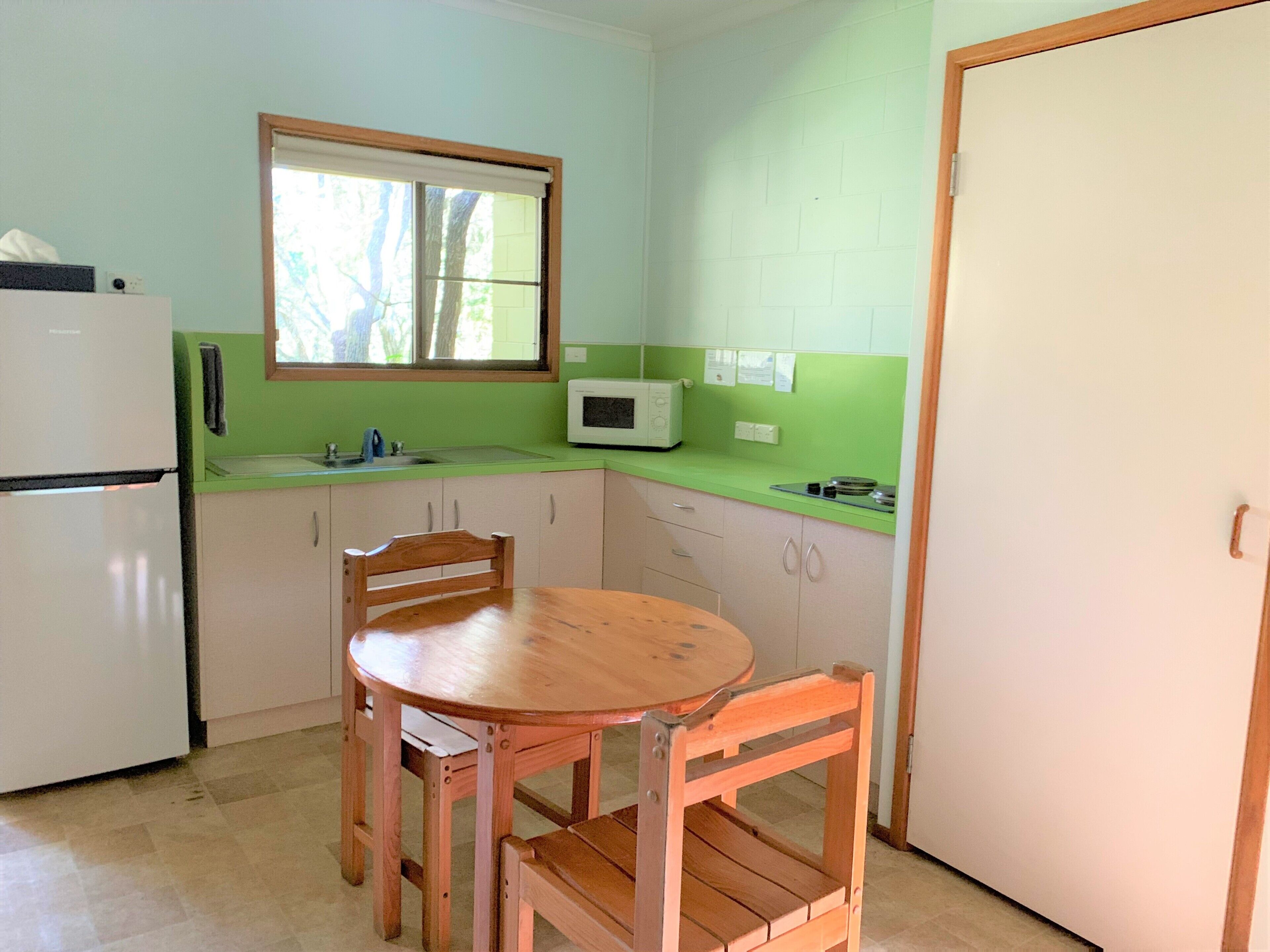 A compact kitchen with a refrigerator, microwave, sink, and wooden dining table.