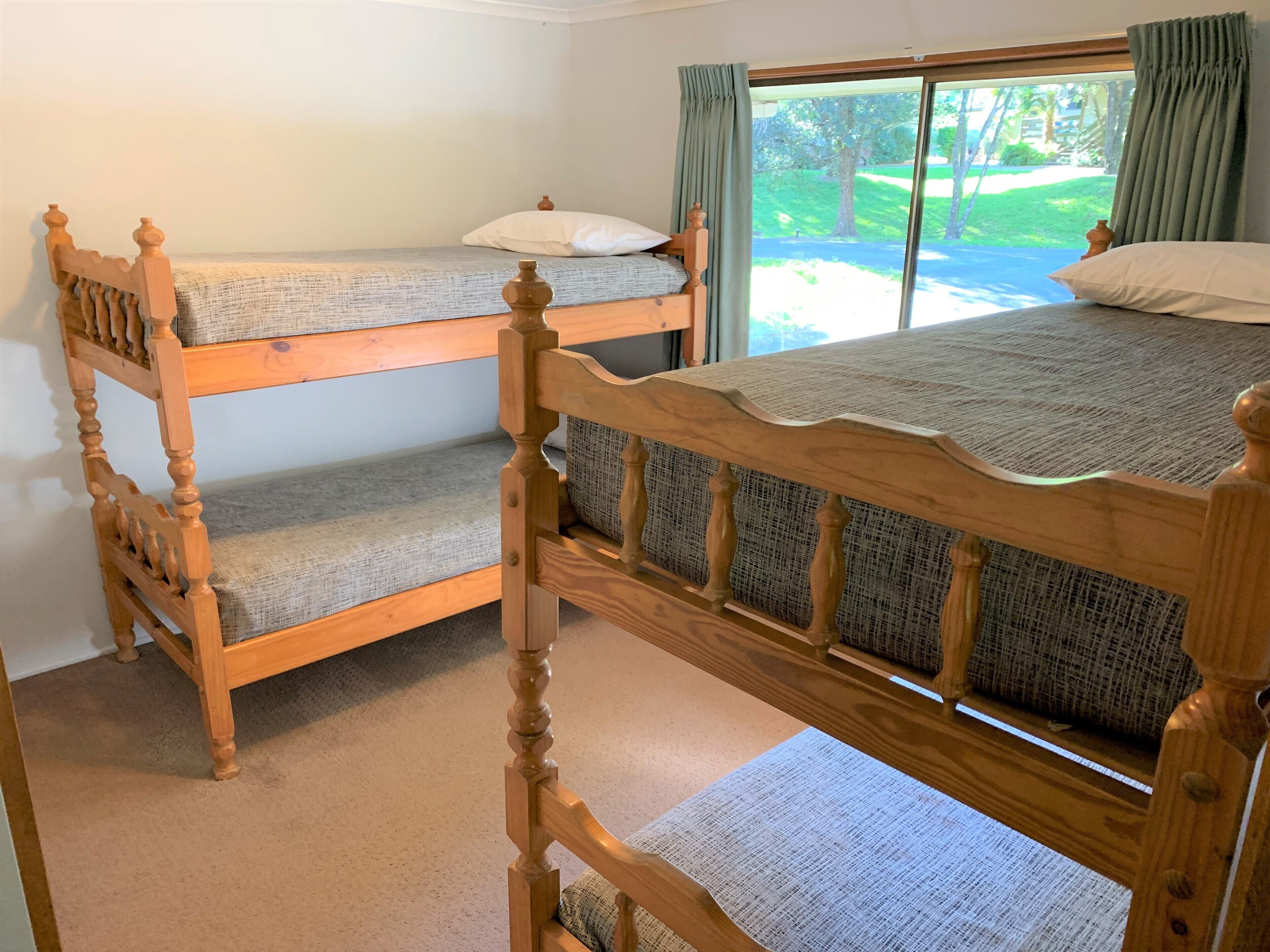 A room with two wooden bunk beds, a window with curtains, and a view of a green landscape.